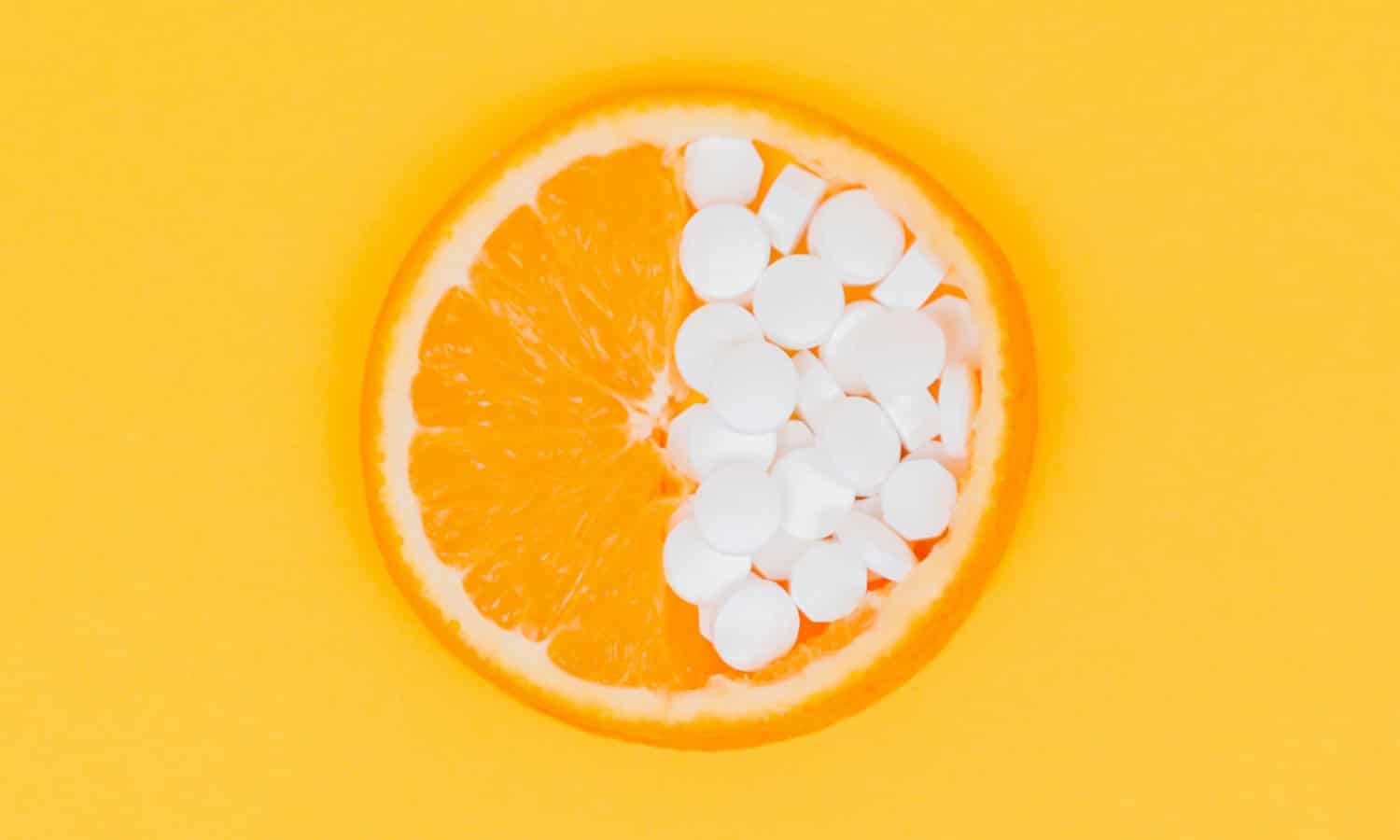 An orange slice with white pills covering half of the slice, against a yellow-orange backdrop