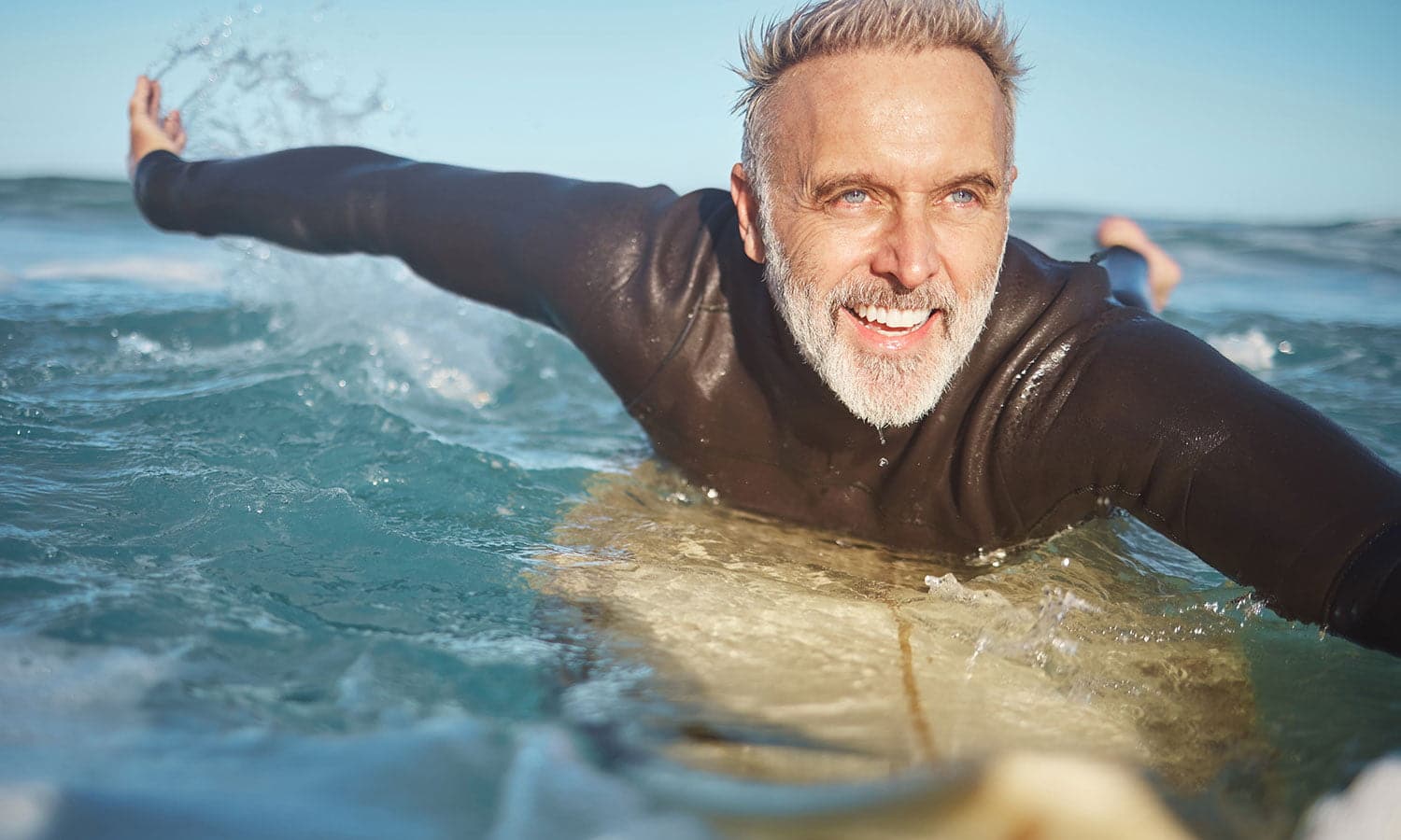 older man swimming on surfboard while on Testosterone Replacement Therapy